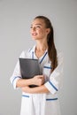 Beautiful happy young woman cosmetologist doctor isolated over grey wall background holding folder