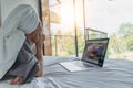 Beautiful happy young woman in a gray bathrobe and with a towel on her head on a bed in a hotel room working on a laptop, vacation Royalty Free Stock Photo