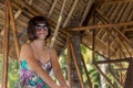 Beautiful happy young woman in sunglasses sitting in a wooden gazebo at sunny day. Tropical Bali island, Indonesia. Royalty Free Stock Photo