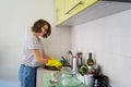 Beautiful happy young woman washing dishes in the sink at home in yellow gloves, cleaning the house Royalty Free Stock Photo