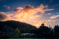 Beautiful HDR scene of late sunset with flaming sky over darken ground and silhouettes of foresty hills. Small farmhouse Royalty Free Stock Photo