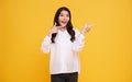 Beautiful healthy Asian young woman smiling with his finger pointing and looking at on light yellow background Royalty Free Stock Photo