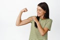 Beautiful and healthy athletic woman, showing muscles, flexing bicep and smiling, looking at her strong arm, standing
