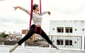 Beautiful healthy strong woman wearing sport bra, relaxing, exercise yoga fly in air, aerial hoop on outdoor rooftop in morning. Royalty Free Stock Photo