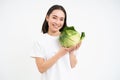 Beautiful and healthy young woman smiling, showing green cabbage, organic lettuce, white studio background Royalty Free Stock Photo