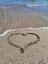 Beautiful heart drawn on the beach sand near the sea water. Vacation, love concept Royalty Free Stock Photo
