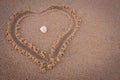 Beautiful heart symbol in beach sand with sea shell in middle. Focus set on seashell Royalty Free Stock Photo