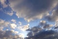 Beautiful heaven landscape with dense stormy white and gray clouds on different levels against the sun on the sky