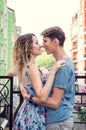 Beautiful heterosexual couple hugging on the balcony. Multicolored urban houses on the background.