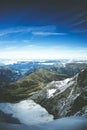 Beautiful high angle shot of green mountains covered in snow under the blue cloudy sky Royalty Free Stock Photo