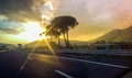 Beautiful highway landscape view on road, mountains and trees on golden sky background with pink clouds and sun rays