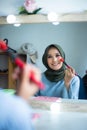 Beautiful hijab woman is dressing up in front of the mirror while holding brush. Hijab girl at makeup room Royalty Free Stock Photo