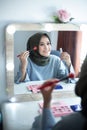 Beautiful hijab woman is dressing up in front of the mirror while holding brush and lipstick. Hijab girl at makeup room Royalty Free Stock Photo