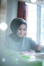 Beautiful hijab woman is dressing up in front of the mirror while holding brush for makeup. Hijab girl at makeup room Royalty Free Stock Photo