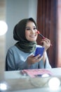 Beautiful hijab woman is dressing up in front of the mirror while holding brush and powder. Hijab girl at makeup room Royalty Free Stock Photo