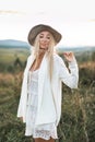 Beautiful hippie girl holding dried spike grass, wearing white clothes, dress and jacket in boho style, hat, walking in Royalty Free Stock Photo