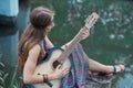 Beautiful hippie girl playing guitar near forest lake Royalty Free Stock Photo