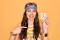 Beautiful hippie woman with blue eyes wearing sunnglasses holding peace symbol reminder with surprise face pointing finger to