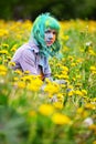 Beautiful hipster alternative young woman with green hair sits in grass with dandelion in park Royalty Free Stock Photo