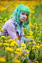 Beautiful hipster alternative young woman with green hair sits in grass with dandelion in park Royalty Free Stock Photo