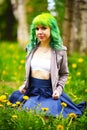 Beautiful hipster alternative young woman with green hair sits in grass with dandelion in park Royalty Free Stock Photo