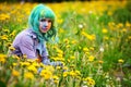 Beautiful hipster alternative young woman with green hair sits in grass with dandelion in park Royalty Free Stock Photo