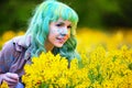 Beautiful hipster alternative young woman with green hair sits in grass with dandelion in park Royalty Free Stock Photo