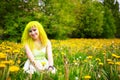 Beautiful hipster alternative young woman with yellow hair sits in grass with dandelion in park Royalty Free Stock Photo