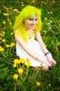 Beautiful hipster alternative young woman with yellow hair sits in grass with dandelion in park Royalty Free Stock Photo