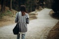 Beautiful hipster girl with black leather purse walking down pavement road in the countryside, young woman tourist in stylish