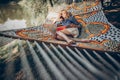 Beautiful hipster girl lying on a hammock and reading a book, camping leisure, stylish woman resting outdoors near a lake on a Royalty Free Stock Photo