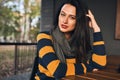 Beautiful hipster girl wears sweater sitting outdoors at cafeteria while waiting friends. Happy young woman sitting outdoors in Royalty Free Stock Photo