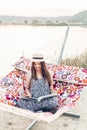 Beautiful hipster woman relaxing in a hammock, emotional girl in stylish hat reading book while resting on the beach at sunset Royalty Free Stock Photo