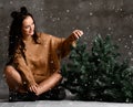 Beautiful hipster woman sitting with Christmas fir tree in knitted sweater blouse under snow Royalty Free Stock Photo