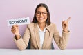 Beautiful hispanic business woman holding economy message paper smiling happy pointing with hand and finger to the side