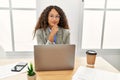 Beautiful hispanic business woman sitting on desk at office working with laptop looking confident at the camera with smile with Royalty Free Stock Photo