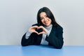 Beautiful hispanic business woman sitting on the table smiling in love showing heart symbol and shape with hands Royalty Free Stock Photo