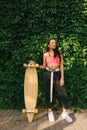 Beautiful hispanic girl posing at camera with skate in hand on green background. Street style.Stylish mulatto girl stands with