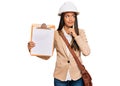 Beautiful hispanic woman architect showing black space on clipboard serious face thinking about question with hand on chin,