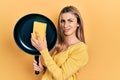 Beautiful hispanic woman cleaning cooking pan with scourer clueless and confused expression