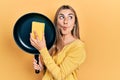 Beautiful hispanic woman cleaning cooking pan with scourer making fish face with mouth and squinting eyes, crazy and comical