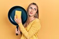 Beautiful hispanic woman cleaning cooking pan with scourer smiling looking to the side and staring away thinking