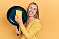 Beautiful hispanic woman cleaning cooking pan with scourer sticking tongue out happy with funny expression