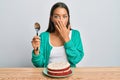 Beautiful hispanic woman eating carrot cake covering mouth with hand, shocked and afraid for mistake Royalty Free Stock Photo