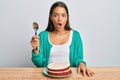 Beautiful hispanic woman eating carrot cake scared and amazed with open mouth for surprise, disbelief face Royalty Free Stock Photo