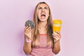 Beautiful hispanic woman eating doughnut and drinking coffee angry and mad screaming frustrated and furious, shouting with anger Royalty Free Stock Photo
