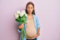 Beautiful hispanic woman expecting a baby holding flowers making fish face with mouth and squinting eyes, crazy and comical