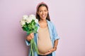 Beautiful hispanic woman expecting a baby holding flowers smiling and laughing hard out loud because funny crazy joke Royalty Free Stock Photo