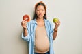 Beautiful hispanic woman expecting a baby, holding food making fish face with mouth and squinting eyes, crazy and comical