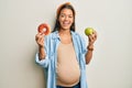 Beautiful hispanic woman expecting a baby, holding food smiling and laughing hard out loud because funny crazy joke Royalty Free Stock Photo